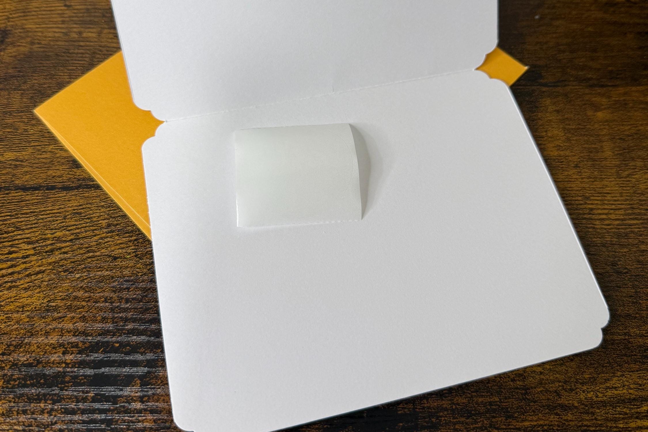 White card with a square cutout on a wooden surface