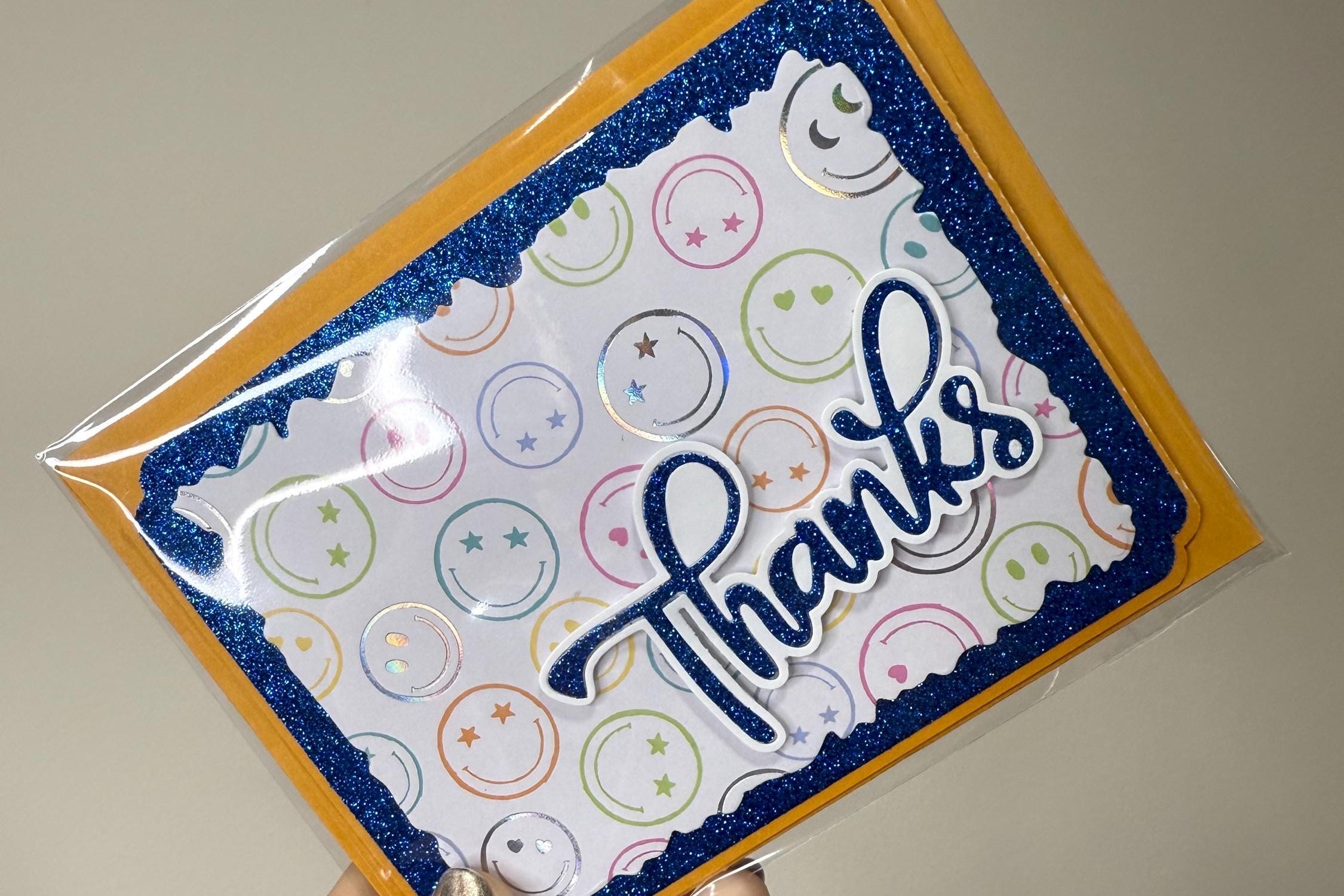 Hand holding a card with 'Thanks' text and smiley face design.