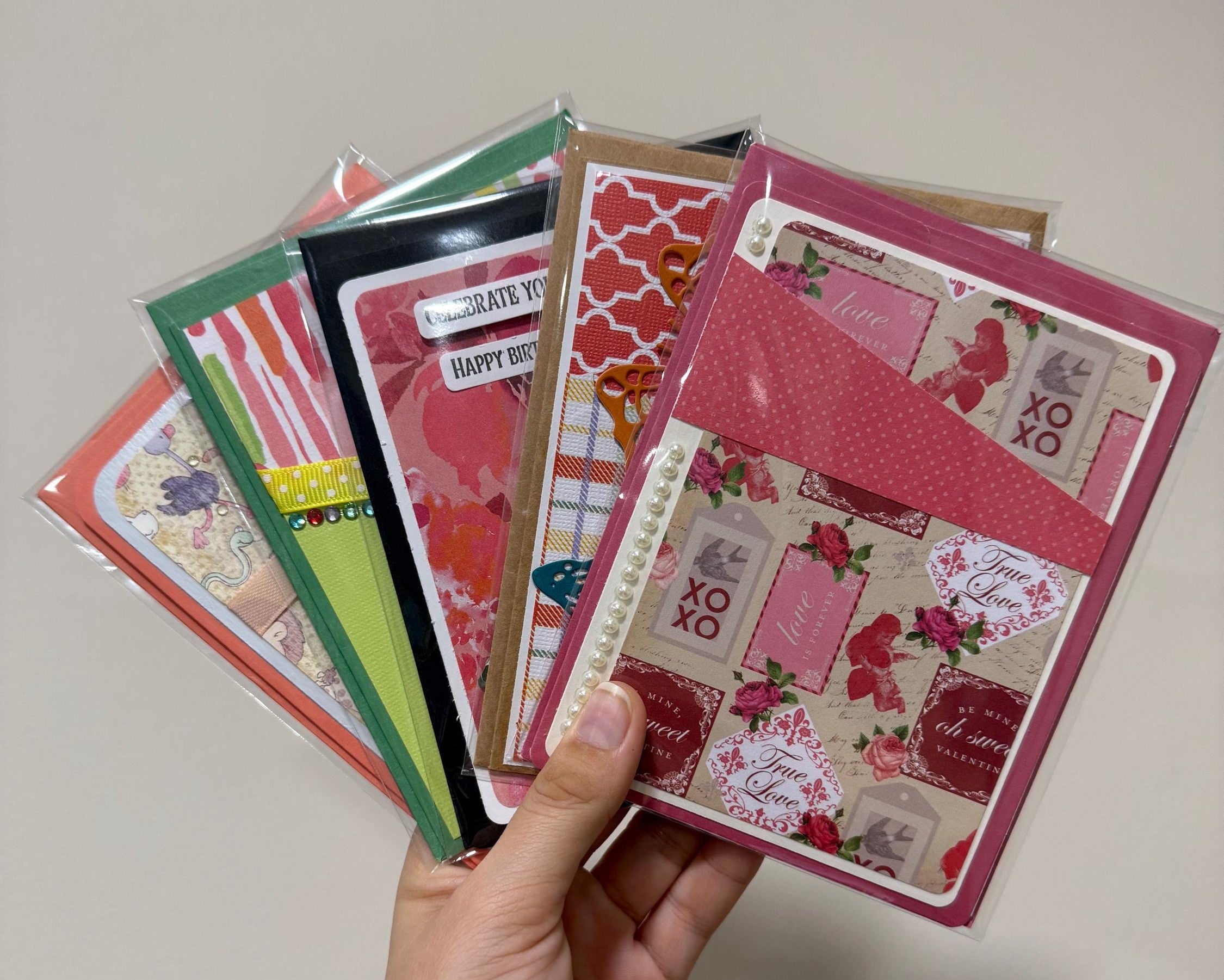 Hand holding a collection of greeting cards with various designs on a plain background