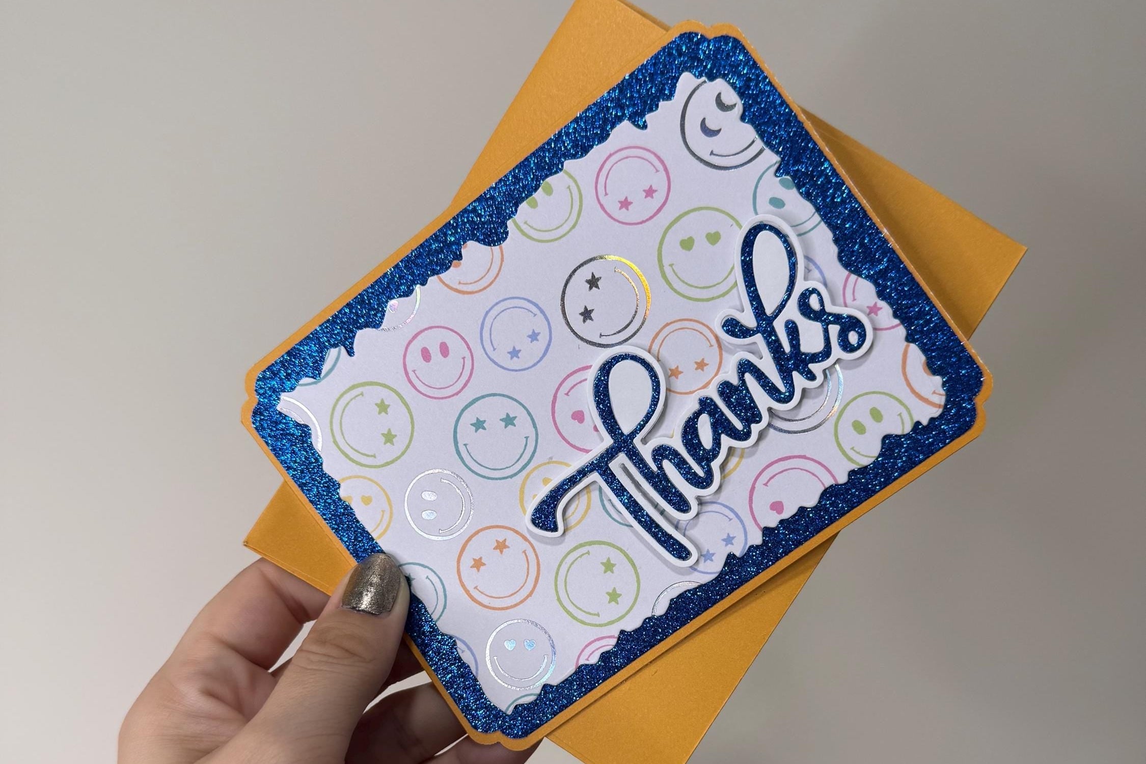 Hand holding a card with 'thanks' and smiley faces on a plain background