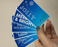 Hand holding blue holiday cards with white text against a beige background